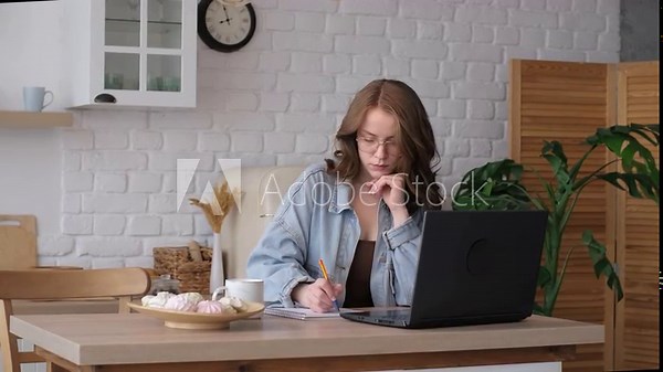 With a serious expression, a woman types away at her laptop in a well-appointed kitchen. The image portrays the new normal of domestic work environments.