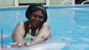African mature woman having fun in swimming pool during summer vacations. Luxury travel vacations
