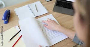 Female language editor opens script lying on wooden table with laptop in office premise. Actress looks for own role lines. Concept of preparing for speech slow motion