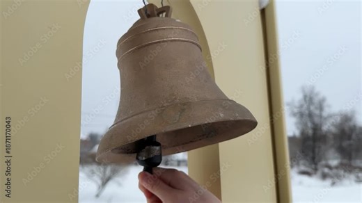 Hand Ringing Large Brass Bell in Outdoor Setting.Close-up image of a hand ringing a large brass bell outside. The bell is prominently displayed, with the hand gripping the clapper.