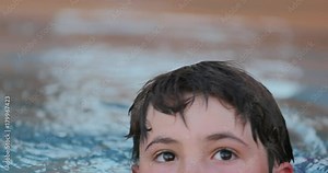 Child doing waves with hands inside swimming pool water. Young boy playing by himself inside swimming pool in 4k clip 60fps resolution