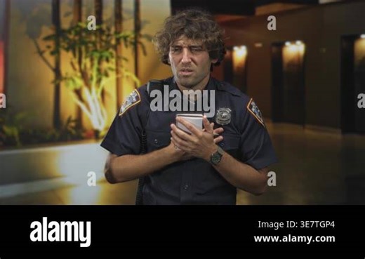 Man police officer writing in notebook with pen, hand on chest, shoulder radio and badge visible in building lobby corridor; duty concern Stock Video Footage - Alamy