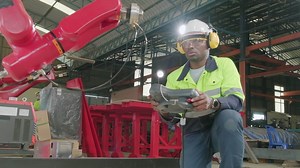 Download An African American production engineer test and control robotic arm in mechanical manufacturing factory, intelligent automatic machines in industrial business, and futuristic technology innovation. for free