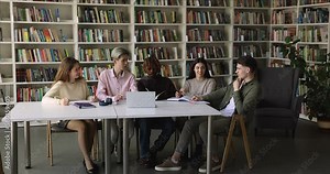 Diverse high school students brainstorming on class project in library, sitting at table with laptop together, talking, discussing study research, writing notes, enjoying teamwork