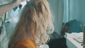 Slow motion, close up, Hairdresser makes bouffant on the hair of young blond woman, use a comb. Stylist fixes the hairstyle with hairspray. Fashion hairdresser does hairstyle to the client. Side view