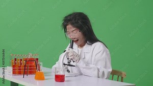 Side View Of Crazy Asian Woman Scientist Looks Through A Microscope On Table With Test Tube Smiling And Saying Wow While Sitting In The Green Screen Background Laboratory