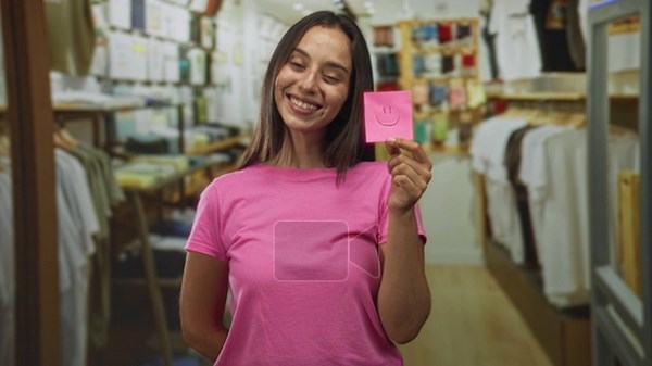Woman holding a pink sticky note with a drawn smile in a clothing store building, smiling at the note; happiness positivity Stock Video Footage - Alamy