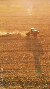 Tractor moving on agricultural field and plowing soil for seeding cereals, growing soybeans, aerial view. Fascinating agricultural scenery in sowing season, bright sun and shadow of machinery on land