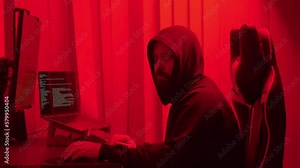 Hacker in hood cracking code using laptop from his dark hacker room