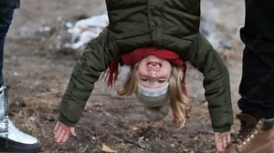 young parents hold their happy daughter by her legs upside down. A little girl hangs upside down in her parents' arms. Family walk in the park.