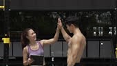 Man climbing monkey bar outdoor for exercise with female trainer.