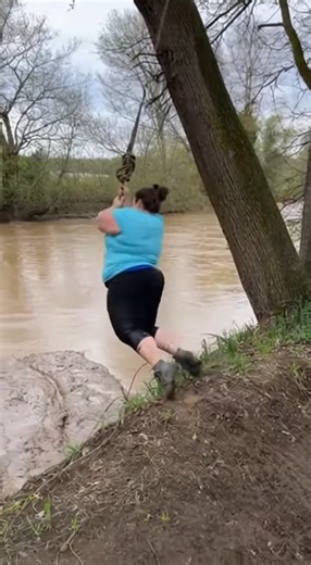 Rope Swing Fails After Being Secured to Flimsy Branch, Chaos Ensues Athens, Georgia. Handheld footage shows a swollen, muddy river running through a wooded area as a person prepares to use a rope swing tied high on a tree along the bank to swing around the tree. The setup appears improvised, with the rope anchored to a thin branch extending over the water. Moments into the clip, the individual grabs the rope and launches outward from the bank. As their weight shifts fully onto the swing, the bra