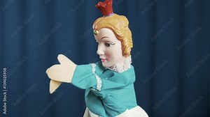 Princess in blue dress and red crown hand puppet toy rubbing and shaking arms, waving on scene with blue crease curtains background