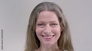Pretty senior woman with loose hair laughs expressing happiness on light grey background closeup. Smiling senior lady shows positive emotion slow motion. Cheerful healthy female person pensioner