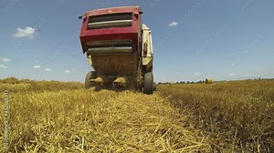 Hay Baling Machine Unloading Cylindrical Bale of Hay - Tractor with Baling Machine Working in a Harvested Wheat Field