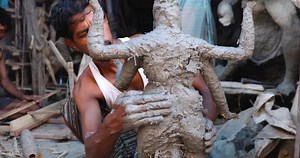 Kumartuli, India- 17 Sep 2020- An eye level view of an artisan prepping the structure of Maa Durga Idol by applying clay or ‘Ganga Matti’ at his workshop. Two other artisans can be seen behind.
