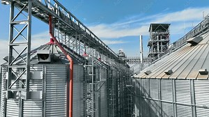 Grain storage facility with metal structures and blue sky. A modern grain storage facility featuring large metal silos connected by a network of metal walkways and pipelines.