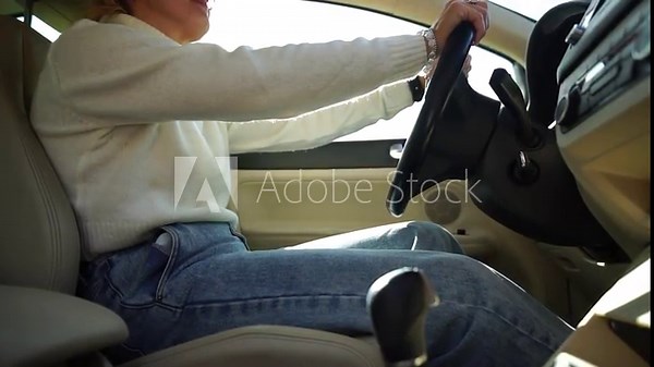 Woman start car. Happy joyful lady blonde hair smiles get in automobile with white leather salon turns ignition key holding hand on steering wheel against green trees. close up cabin view, slow motion