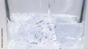 Cold sparkling fizzy tonic water with bubbles pouring into a glass with ice cubes. Refreshment carbonated soft drink or beverage close up