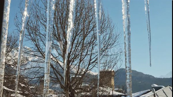 Mestia Georgia view through icicles with Svan towers and snowy mountains in background at sunrise. Mestia village traditional guesthouse. Svan towers house. Morning sunrise window view hotel panorama