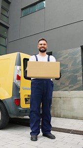 Delivery man holding cardboard box near van