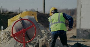 Male construction worker putting cement in mixer with shovel