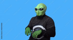 Professional artist in alien costume and in a black t-shirt laughs and clutches his head in hysteria against blue chromakey background. Role rehearsal.