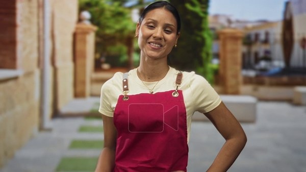 Woman in red apron makes call gesture with hand to ear on a sunlit street plaza with stone columns and tiled walkway; friendly invitation Stock Video Footage - Alamy