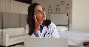 Pensive female cardiologist in medical coat looking at computer screen, thinks of problem solution, ponders, consulting patient through e-health, working in hospital office. Workflow, tech, medicine