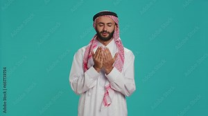 Islamic man praying to allah in studio, having hope in religious ritual over blue background. Middle eastern person worshipping God with meditation, faithful muslim devotion.