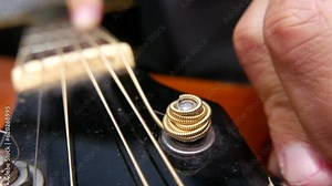 Tightening the strings of a guitar. Tuning a guitar. Musician changing guitar strings. Man adding new strings to a guitar. Musician testing guitar strings. Acoustic guitar, close-up angle: guitar neck