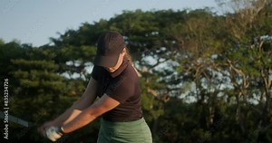 Portrait of a young attractive woman in a cap playing golf at a country club. She swings the golf club and hits the ball, then she looks into the distance with concentration to see how hits the hole.