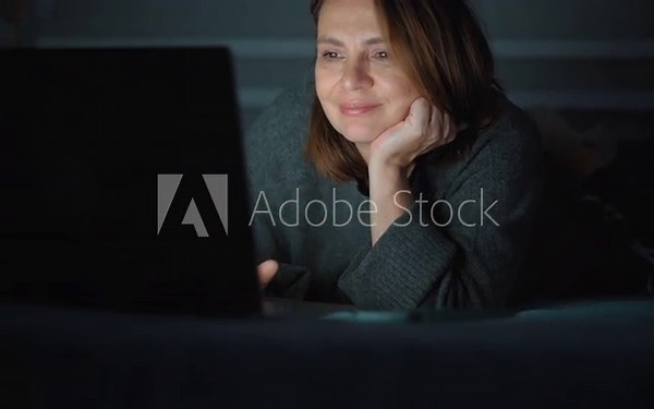 An adult internet addict woman networking concentrated late at night in bed with a laptop