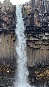 A waterfall cascades down hexagonal basalt columns in a close vertical view