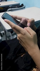 Woman hand touching and scrolling mobile phone screen in classroom.