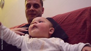 Father is immitating sounds that his six months old baby boy is making while tickling his feet. Baby is making funny faces and kicking with his feet