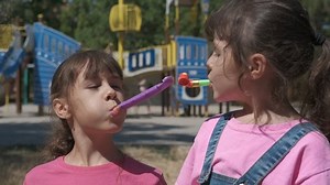 Blow in party horns. Children make noise with party horns on the sunny playground.