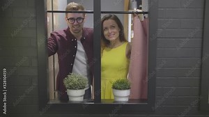 Young couple in love opening curtains and looking out the window