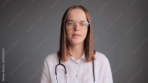 Confident woman doctor wearing white lab coat and stethoscope standing isolated over grey background gesturing while explaining disease treatment professional advice for health care.