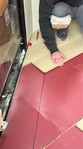 installing light wood laminate flooring planks over a red underlayment surface in the indoor room