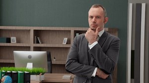 Un homme d'âge mûr aux cheveux gris fin en tenue formelle, pensant au problème de se tenir debout dans un bureau spacieux et bien meublé. Un homme sérieux qui résout le problème en tête. Vidéos 4k de grande qualité