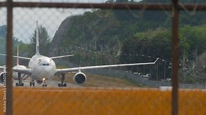 Airplanes taxiing on the tarmac of Phuket Airport, view through the airport fence