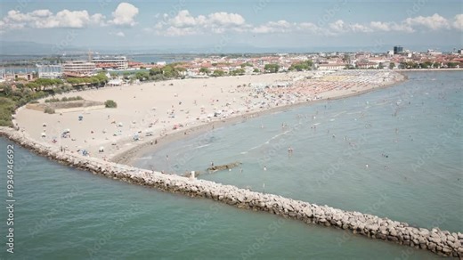 Smooth 4K UHD drone pulls back from the Grado sandy beach, revealing a stone jetty and the expansive Adriatic Sea—ideal for travel films and establishing shots.