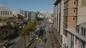 Forwards tracking of historic PCC streetcar driving on Market Street on sunny day. Wide boulevard with row of palm trees.