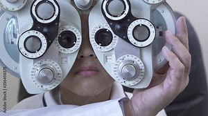 Little boy's eye examination at optometrist ophthalmologist using phoropter close up. Hand of the doctor changing glass on one eye of teen boy on phoropter. Slow motion