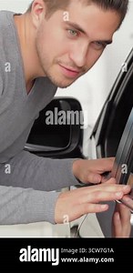 A stylish young man leans in with a gleaming smile, captivated by the glossy finish of his new car in a modern showroom. This vibrant scene radiates excitement and satisfaction, highlighting the joyful connection between a customer and the automotive Stock Video Footage - Alamy