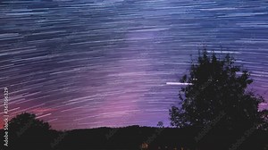 Star trail Time-lapse 4k footage of the stars behind a lone tree in the night sky. Milky Way galaxy orbiting over a mountain