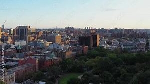 Aerial footage towards Marcus Garvey / Mount Morris Park in the Harlem Neighborhood of NYC at golden hour sunrise. The mighty George Washington Bridge is visible in the distance. in 4K.