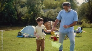Grandson and grandfather look at nature and talk while walking in a meadow during a family summer trip in nature