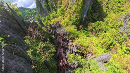 Woman walking a long suspended canopy bridge high above lush green jungle and tropical limestone cliffs of El Nido, Palawan. Enjoying adventure and exploring nature in the Philippines